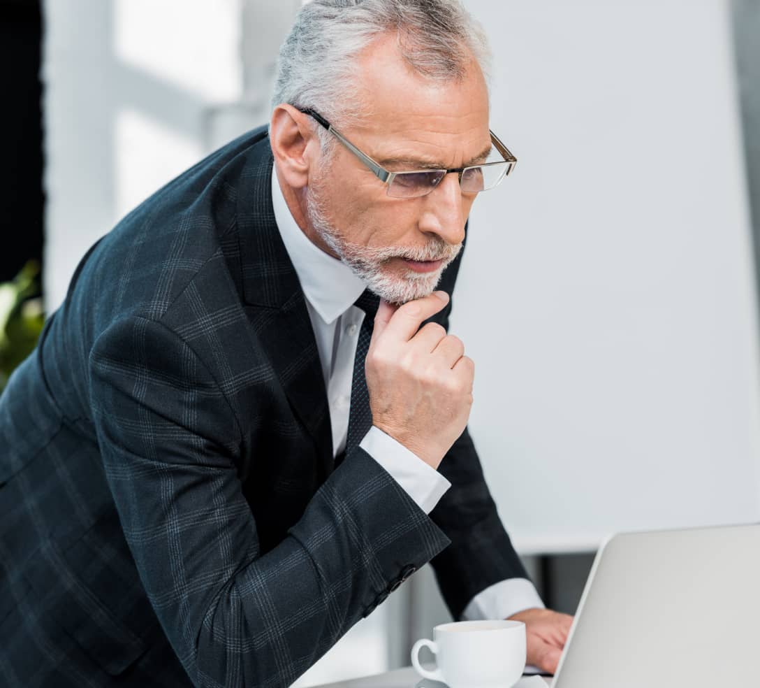 Grey-haired man thinking and looking at a laptop