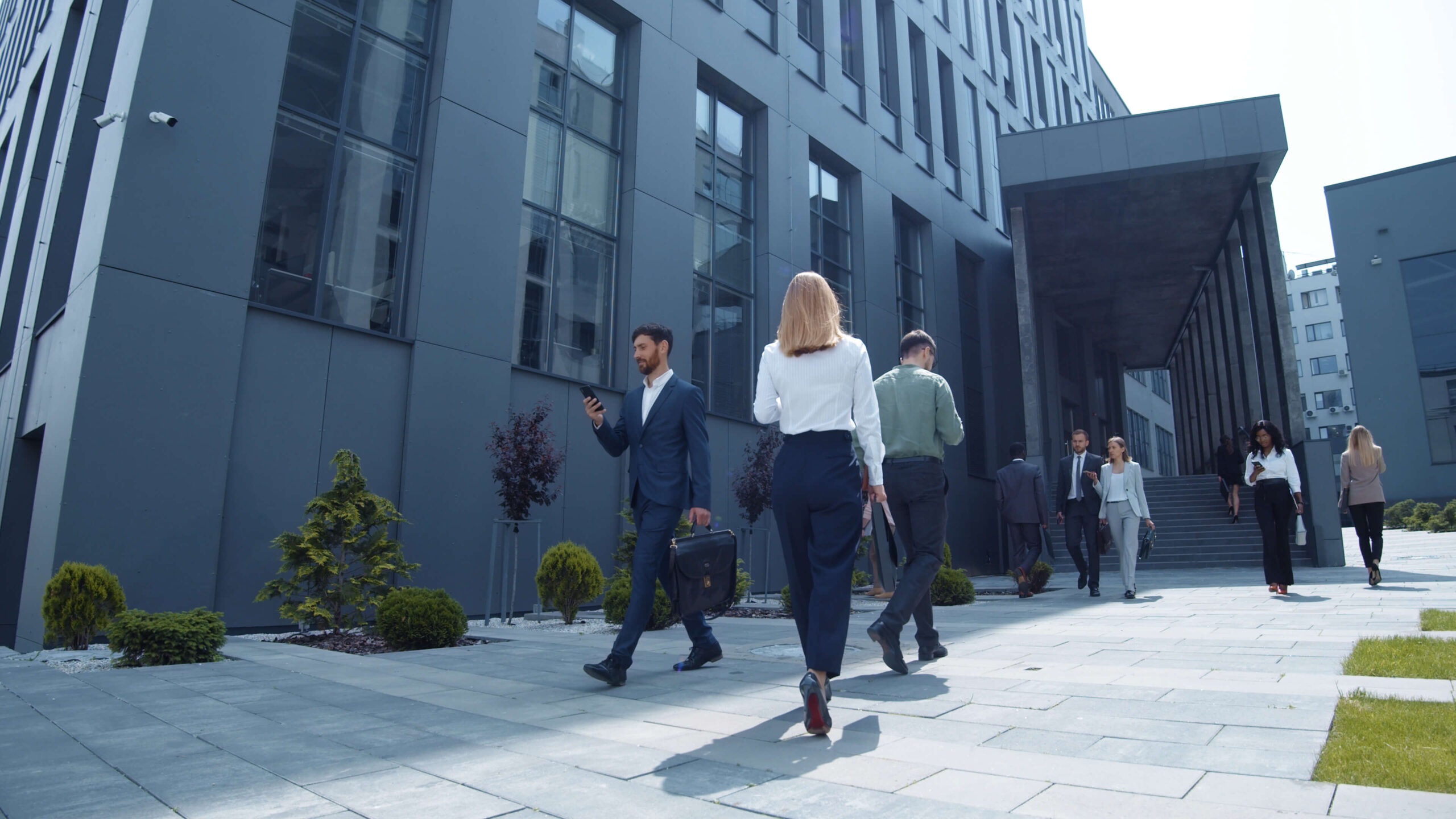 Well-dressed people walking near a corporate building.