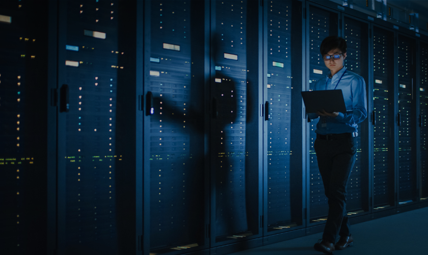 Man walking next to servers with a laptop